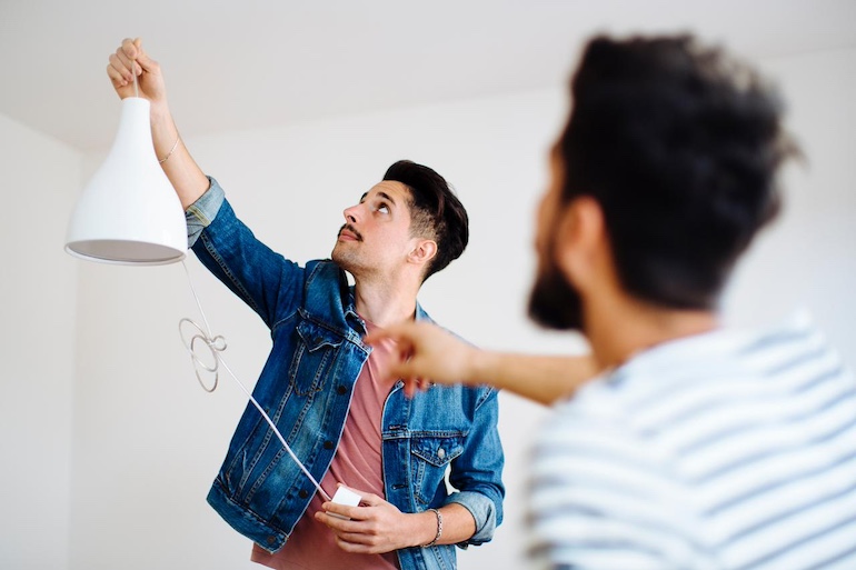 Vermietung ohne Energieausweis: welche Konsequenzen drohen? Ein Mann hält eine Deckenlampe hoch, die noch nicht angeschlossen ist, ein anderer ist von hinten zu sehen