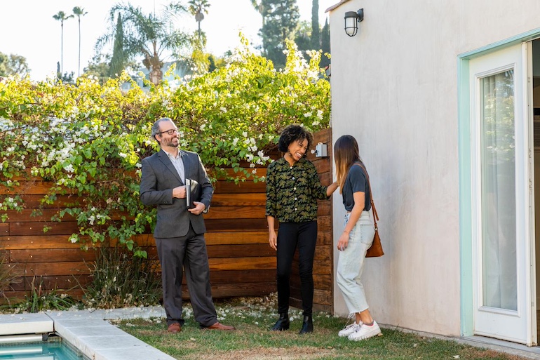 Mietvertrag für Einliegerwohnung Makler, Vermieterin und Mieterin stehen im grünen Garten mit Pool der Einliegerwohnung nach erfolgreicher Besichtigung.